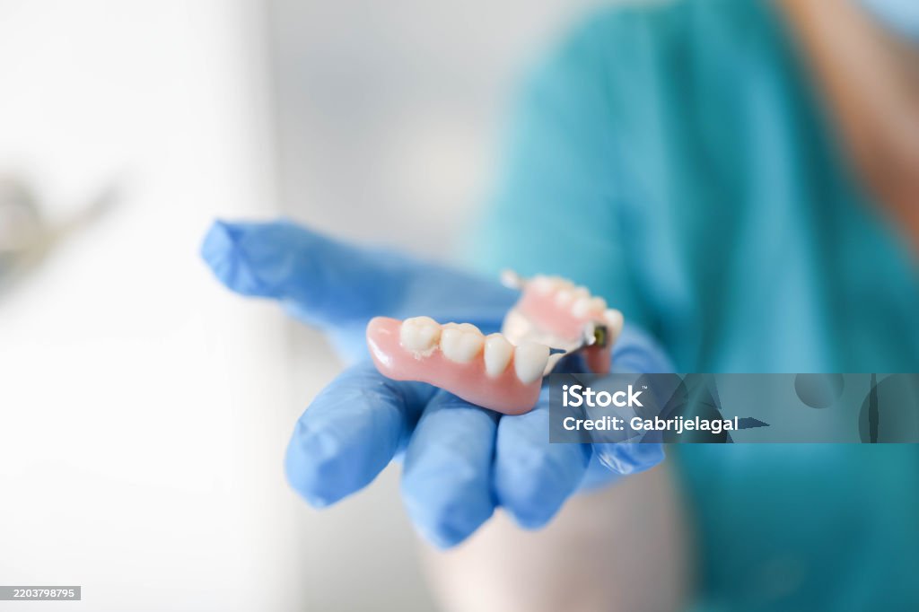 A dentist is holding a detailed wax dentures model in their hand, carefully examining its structure and alignment.